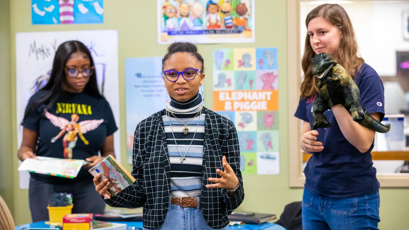Three Duquesne Education students are presenting a teaching lesson presentaton in the library with a puppet, lesson plan and book.